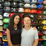Owners of baseball cap store in front of cap wall